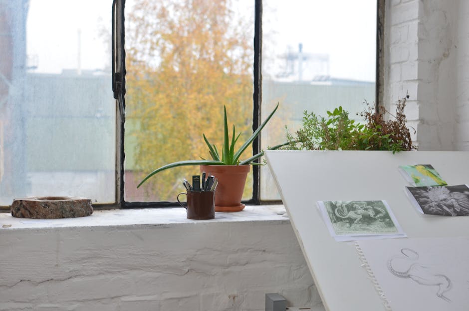 Interior of art studio with green plants near table with pictures and sketch