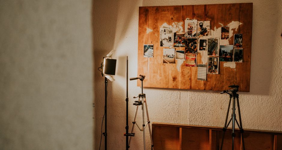 Photography studio corner with lighting equipment and collage board on the wall.